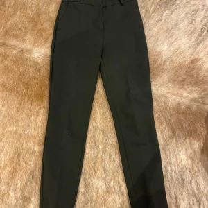 Svarta kostymbyxor - Snygga svarta kostymbyxor i klassisk stil. De har en rak passform och är perfekta för både formella och semi-formella tillfällen. Byxorna har hällor för bälte och diskreta fickor både fram och bak. Ett måste i garderoben för en stilren look!