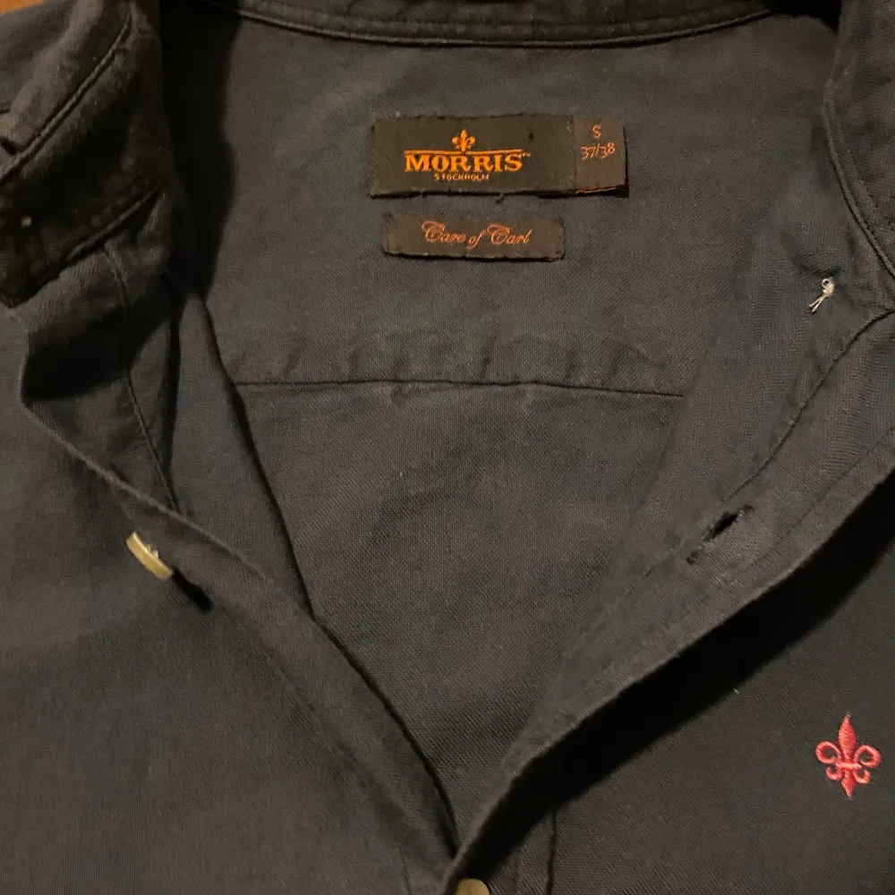 Fin blå/ljusblå skjorta med rosa/ljusrött märke från morris, köpt secondhand och aldrig använd sen dess, i princip nyskick syns inga tecken på användning. Paidat.