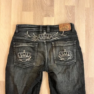Svarta jeans med broderade detaljer - Säljer ett par snygga lågmidjade mörkblå jeans från Miss O&y. De har coola broderade kronor på bakfickorna och en unik design på baksidan. Jeansen är bootcut och stretchiga.