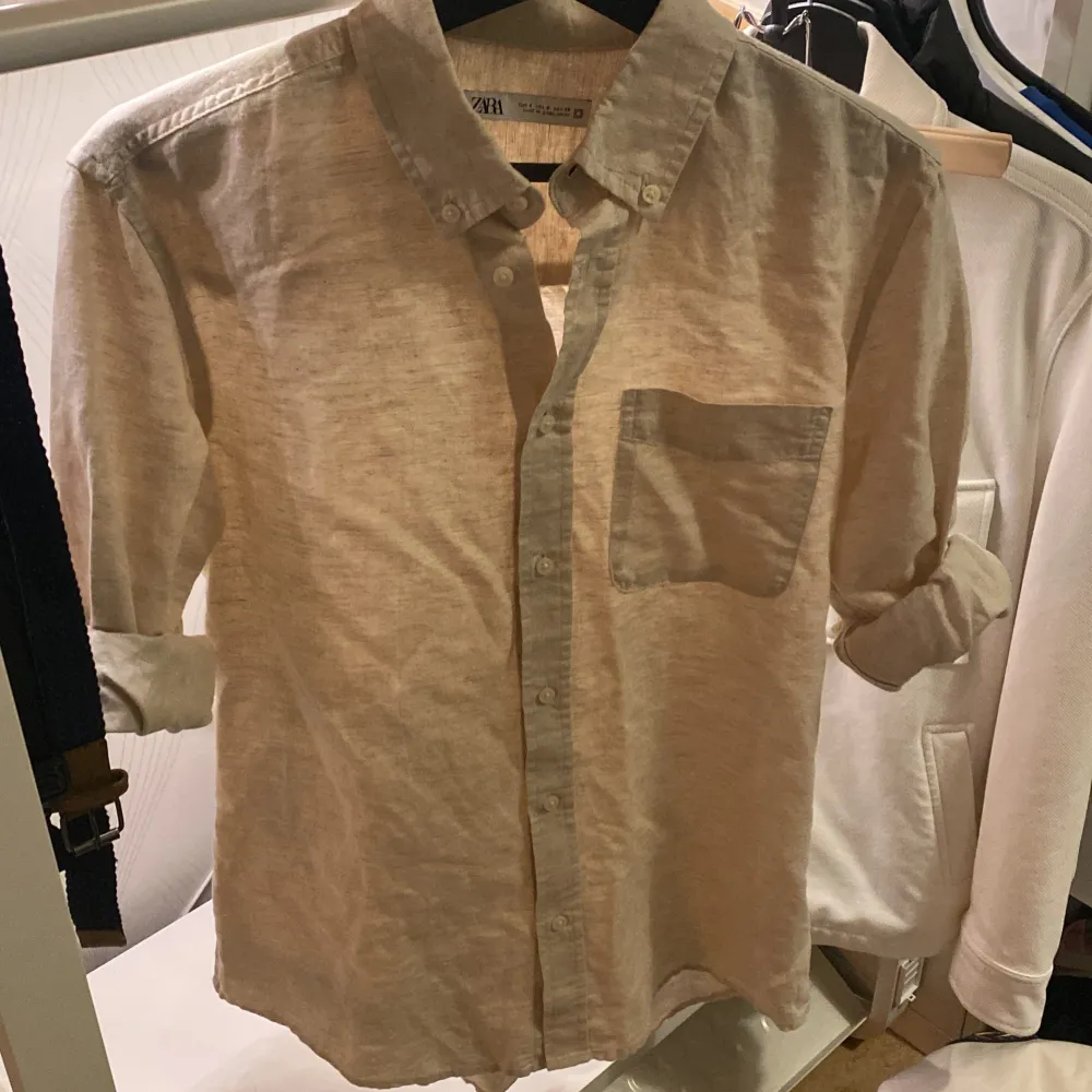 Säljer en stilren beige skjorta från Zara i storlek S. Skjortan är långärmad och har en klassisk krage med knappar framtill. Den är tillverkad i ett lätt och bekvämt material, perfekt för både vardag och fest. Skjortan har en bröstficka som ger en extra touch av stil.. Skjortor.