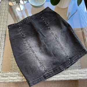 Svart jeanskjol från Zoul - Säljer en svart jeanskjol från Zoul i storlek 34. Kjolen har dragkedja bak och är dekorerad med små nitar framtill. Materialet är 98,6% bomull och 1,4% spandex, vilket gör den både bekväm och stretchig. Säljs enbart för att jag vuxit ur den. En personlig favorit ❤️ 