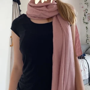 Rosa halsduk - Säljer en superfin rosa halsduk som är perfekt för att hålla sig varm och snygg under kyliga dagar. Den är lång och kan lindas flera varv runt halsen för extra mysfaktor. Passar perfekt till både vardag och fest!