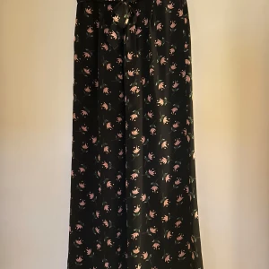 Blommig långkjol från Twist & Tango - Snygg byxkjol från Twist & Tango med ett vackert blommönster i rosa och grönt på en svart bakgrund. Kjolen har en knytning i midjan för en justerbar passform. Perfekt för en stilfull look.