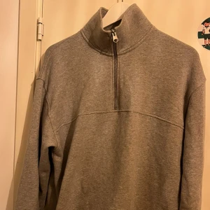 Grå tröja med dragkedja - Säljer en grå tröja med halv dragkedja och hög krage. Perfekt för kyliga dagar med sin bekväma passform och långa ärmar. Enkel och stilren design som passar till det mesta.