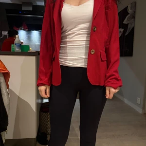 Röd kavaj med knappar - Snygg röd kavaj med två knappar framtill och fickdetaljer. Perfekt för att ge en färgklick till din outfit. Kavajen har en klassisk passform och långa ärmar. Stolek 38. Ifrån Lindex.