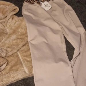 Beige byxor med leoparddetalj - Snygga beige byxor med en cool leoparddetalj i midjan. Perfekta för en trendig look. Byxorna har en rak passform och är tillverkade i ett bekvämt material. Set mysiga byxor och mysig tröja