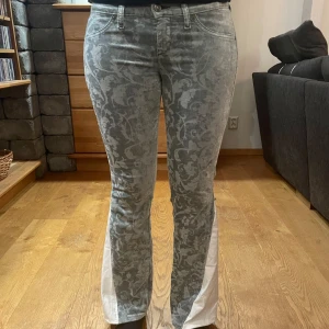 Grön/grå  mönstrade jeans med vita detaljer - Snygga  jeans med ett unikt mönster och vita inslag längs benen.👖De har en klassisk femficksdesign och knäppning fram. Perfekta för dig som vill sticka ut med stil. ⭐️Dem är omsydda av oss! Bootcut och lågmidjade! Innerbensmåttet är 74 cm och midjemåttet är 72 cm!⭐️