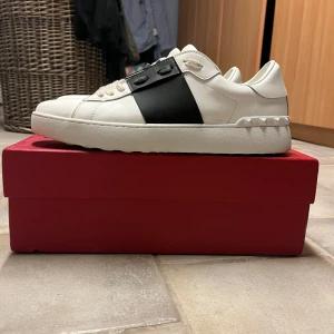 Valentino Garavani sneakers - Snygga Valentino Garavani sneakers i vitt och svart. Skorna har en stilren design med snörning och en bred svart rem över ovansidan. Perfekta för en trendig look. De är andvända några gånger bara. Finna ett litet märke på dem som inte går bort. Sick 9/10 pris kan diskuteras 