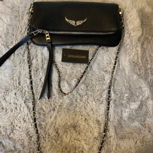 Svart axelväska från Zadig & Voltaire - Snygg svart axelväska i skinn från Zadig & Voltaire med silverdetaljer och kedjerem. Dustbag medföljer och är i bra skick.  