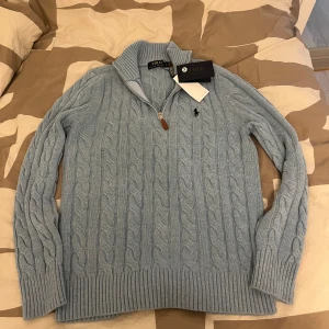 Ljusblå stickad tröja från Ralph Lauren - Säljer en stilren ljusblå stickad tröja från Ralph Lauren med kabelstickat mönster och dragkedja vid halsen. Tröjan har långa ärmar och ribbade muddar. Tröjan är storlek m men passar okcså s Perfekt för kyliga dagar! Tröjan har några defekter som visas på bilderna men om du har frågor eller vill ha fler bilder är det bara at meddela mig😉.