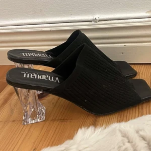 Svarta klackskor från Trendella - Snygga svarta klackskor från Trendella med transparenta klackar. Perfekta för en stilren look. Öppen tå och slip-on design gör dem både trendiga och bekväma.