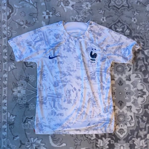 FRANKRIKE FOTBOLLSTRÖJA - Snygg vit fotbollströja från Nike med blått mönster och en tupp på bröstet. Kortärmad design perfekt för match eller träning.