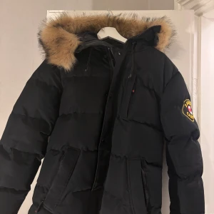  Zavetti Canada (S)/M - Priset är inte hugget i sten! Vid snabb affär går ner i pris. Snygg svart dunjacka från Zavetti Canada med pälsfodrad huva och broderad logga på ärmen.