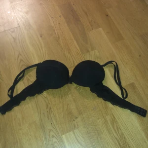 Svart spets-bh - Snygg svart bh med spetsdetaljer och vadderade kupor. Perfekt för en elegant look. Justerbara axelband för bästa passform. Säljer då den är för liten, bara använd en gång.
