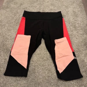 Svarta leggings från Puma - Snygga svarta leggings från Puma med färgglada inslag av rött och rosa. Perfekta för träning eller en aktiv vardag. De har en bekväm passform och är tillverkade i ett stretchigt material.