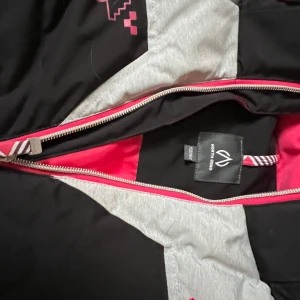 Svart och grå vinterjacka från North Bend - Snygg och funktionell vinterjacka från North Bend i svart och grått med rosa detaljer. Jackan har en dragkedja framtill och en praktisk huva. Insidan är fodrad i rosa för extra värme och stil. Perfekt för kalla dagar och perfekt att åka skidor i. Använd ett fåtal gånger. Stl 158/164