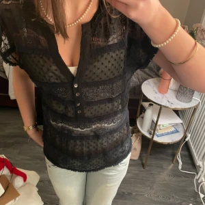 Svart spetsblus - Säljer nu denna as snygga v-ringade, svarta kortärmade blus med såå coola detaljer. Jag har ett vitt linne under då den är ganska genomskinlig. Skulle säga att stl är mellan xs-m beroende på hur man vill att den ska sitta.