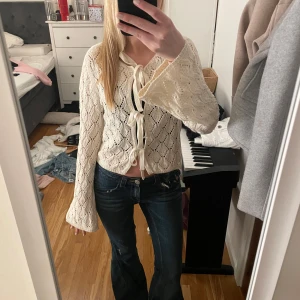 Vit stickad kofta från Stradivarius - Säljer en söt vit/off white stickad kofta från Stradivarius med rosetter framtill. Koftan har ett fint hålmönster och vida ärmar. Köpte den i somras i Italien men har bara använts två gånger! 