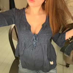 Mörkblå blus från Odd Molly - Säljer en mörkblå blus från Odd Molly med v-ringning och knytband framtill. Blusen har långa ärmar och en smockdetalj vid bysten som ger en fin passform. Perfekt att ha i skolan eller på stan!