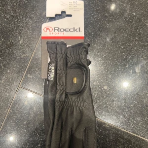 Svarta handskar från Roeckl Sports - Snygga svarta handskar från Roeckl Sports, perfekta för vintern. De har en stilren design med justerbar rem vid handleden för optimal passform. Tillverkade för att ge bra grepp och komfort. Aldrig använda
