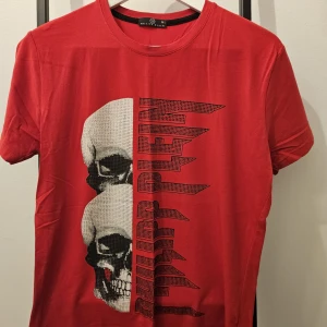 Philipp Plein T-shirt  - Cool röd t-shirt från Philipp Plein med ett stort dödskalletryck och text på framsidan. Perfekt för en edgy stil. Kortärmad och tillverkad i ett mjukt material. HELT NY!