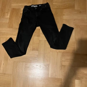 Svarta jeansbyxor - Snygga svarta jeansbyxor med en klassisk design. De har en normal passform och är perfekta för en stilren look. Byxorna har fickor både fram och bak samt en knapp- och dragkedjestängning. Priset kan ändras