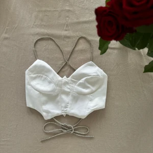 Vit korsettopp - Snygg vit korsettopp med glittriga axelband och knytning i ryggen. Touch av glamour. Toppen är croppad och har en elegant design som framhäver figuren 🤍