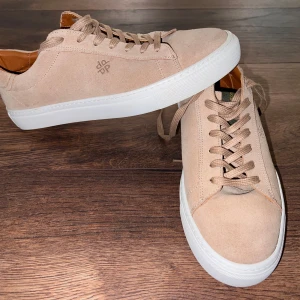 Beige mockasneakers från Playboy - Snygga beige sneakers i mocka från Playboy med vit sula och klassisk snörning. Perfekta för en stilren look.