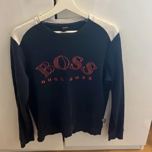  tröja från Hugo Boss - Snygg tröja från Hugo Boss med kontrasterande vita axelpartier och röd logotyp på bröstet. Perfekt för en stilren look.
