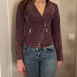 Lila mockajacka från Mexx - Snygg lila mockajacka från Mexx med asymmetrisk dragkedja och knappar framtill. Jackan har en figurnära passform och långa ärmar. Köpte på Secondhand men har redan en liknande. storlek 34🫶