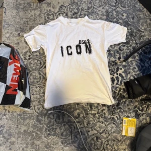 Vit t-shirt med tryck från DSQ2 - Säljer en vit t-shirt från DSQ2 med texten 'ICON' tryckt i svart på framsidan. T-shirten har en klassisk passform och korta ärmar. Perfekt för en avslappnad stil. Pris kan diskuteras