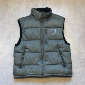 Grön dunväst från Jack & Jones - grön dunväst från Jack & Jones med dragkedja och hög krage. Den är i bra skick utan några problem och väldigt varm 