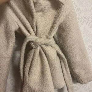 Beige teddyjacka från Vero Moda - Mysig beige teddyjacka från Vero Moda med knytbälte i midjan. Jackan har en klassisk krage och långa ärmar, perfekt för kyliga dagar. Den är både stilren och bekväm, vilket gör den till ett måste i garderoben. Jag kör gärna med Swish ❤️