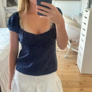 Mörkblå blus med spetsdetaljer - Charmig mörkblå blus med spetsdetaljer vid ärmarna och en söt knappdetalj framtill. Blusen har korta ärmar och en smickrande passform som passar perfekt för både vardag och fest. Köpte på plick men passar tyvärrr inte mig🤗