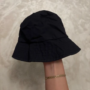 Svart bucket hat - Snygg svart bucket hat i enkel design. Perfekt för att skydda mot solen eller som en stilren accessoar. Passar till många olika outfits och tillfällen. Aldrig använd. 