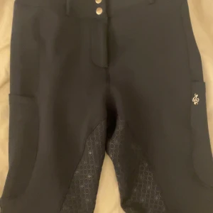 Blåa ridbyxor från ZacZess - Snygga mörk blåa ridbyxor från ZacZess med hög midja och knappar framtill. Byxorna har ett mönstrat grepp på insidan av benen och bak för extra stöd. Perfekta för ridning med praktiska fickor och stilren design.        Använda endast en gång då de inte passade, men de ser helt nya ut! Nypris: runt 1300kr