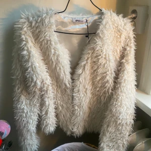 Vit pälsjacka från Gina  - Säljer en fluffig och trendig vit pälsjacka från Gina. Jackan har en öppen design och långa ärmar, perfekt för att hålla sig varm och stilren under kyliga dagar. 