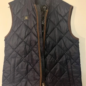 Svart quiltad väst från Morris - Snygg svart quiltad väst från Morris med dragkedja framtill. Perfekt för lager-på-lager under kyligare dagar. Klassisk design med stilren look.