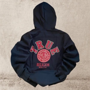 Svart hoodie från True Religion - Helt ny svart hoodie från True Religion med stor logga i rött på ryggen. Storlek L, Nypris 1200kr, mitt pris: 699kr