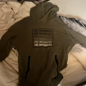 Olivgrön hoodie från Woxd - Säljer en olivgrön hoodie från Woxd med en cool kodgrafik på framsidan. Tröjan har en bekväm passform med långa ärmar och dragkedjor vid fickorna. Perfekt för en avslappnad stil.