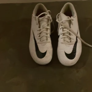 Nike inneskor (futsal) med snörning - Snygga vita Nike fotbollsskor med svarta och röda detaljer. Skorna har en klassisk snörning och en sportig design med Nike-loggan tydligt synlig på sidan. Bästa kvalite