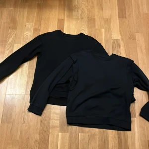 Två svarta tjocktröjor  -  Två svarta tjocktröjor en som är helt svart med ett litet kors där uppe vid halsen och den andra har volanger vid axlarna fina basplagg men ändå fina 
