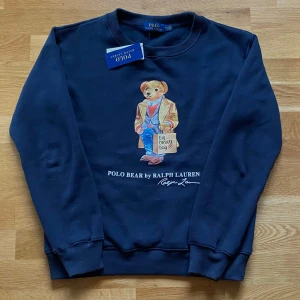 Ralph Lauren Polo Bear mörkblå  - Säljer en mörkblå sweatshirt från Ralph Lauren med det ikoniska Polo Bear-motivet på framsidan. Perfekt för en avslappnad stil med en touch av lyx. Helt ny, lappen hänger kvar. 
