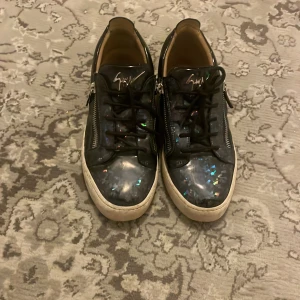 Ett par Guiseppe zannoti med glitter detaljer  - Snygga blå sneakers med glittriga detaljer och snörning. Skorna har en vit sula och dragkedja på sidorna för extra stil och funktionalitet.