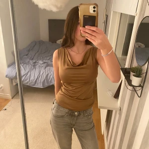 Guld ärmlös topp - Snygg guld ärmlös topp med draperad halsringning. Perfekt för en stilren look. Passar bra till jeans eller kjol.