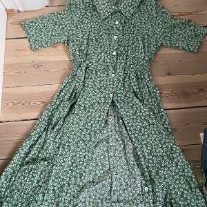 Grön blommig klänning med knappar - Såå fin grön klänning med ett blommor! Klänningen har kortärmade ärmar och knappar framtill. Perfekt för vår och sommar! Jätte skönt material! Skulle gissa att storlek är S/M