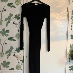 Svart långklänning med v-ringning - Elegant svart långklänning med v-ringad hals och ribbad struktur. Klänningen har långa ärmar och en figurnära passform, perfekt för en stilren look.