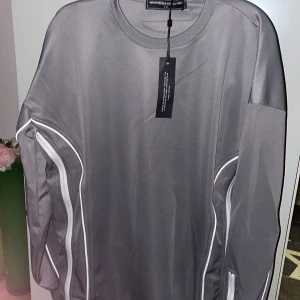 Ny Maniere de voir grå långärmad tröja  Manière De Voir - Snygg grå långärmad tröja från Manière De Voir med vita dragkedjor och detaljer. Ny! Amerikansk märke.Perfekt för en stilren look med en modern touch. Tröjan har en rund hals och är tillverkad i ett mjukt material.