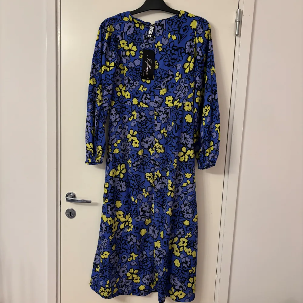 Säljer en färgglad blommig klänning från Influencer i blått och gult. Klänningen har långa ärmar och en vacker blommönsterdesign. Perfekt för att lysa upp garderoben!. Mekot.