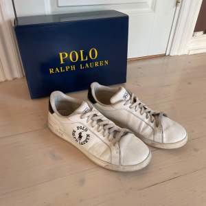 Säljer ett par vita sneakers från Polo Ralph Lauren. De har en klassisk design med snörning och märkeslogga på sidan. Skorna är i skinn och har en svart detalj vid hälen. De är välanvända men fortfarande i bra skick. Perfekta för en laidback stil.😀